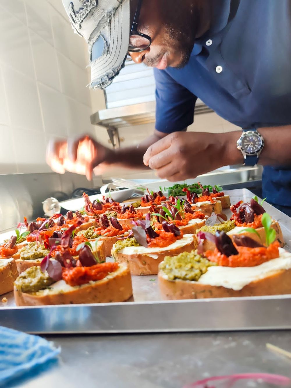 A chef finishing a tray of bruschetta with pesto, romesco and olives